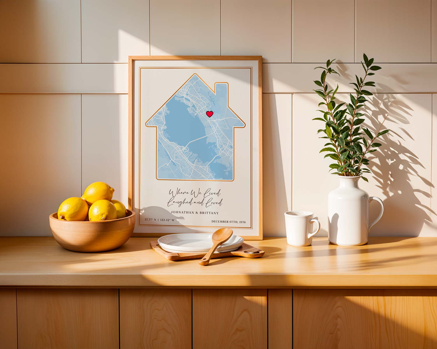 A framed SentiMap print of a home location that means the most to someone on a wooden table with kitchen supplies surrounding the framed print